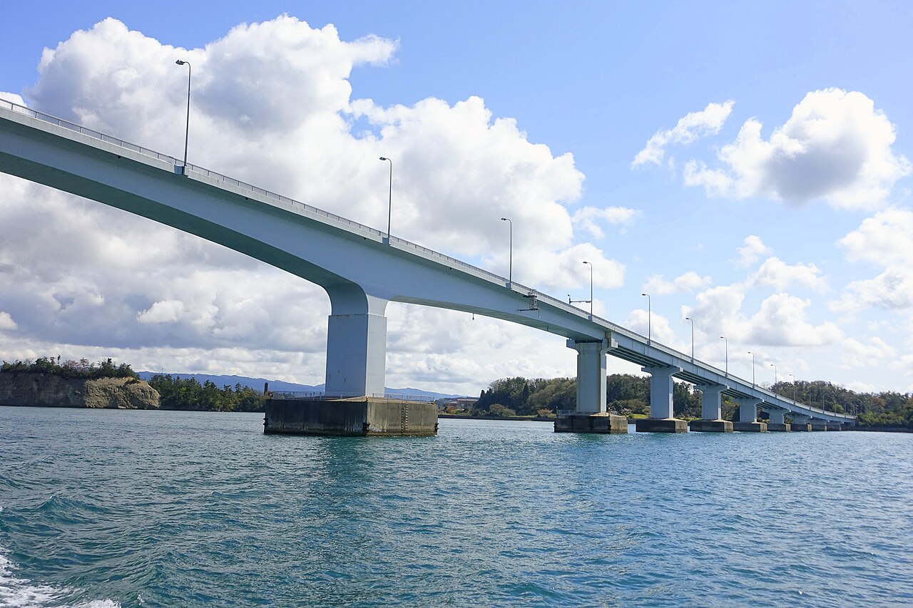 A long white bridge curves gently across the water, seen from a boat