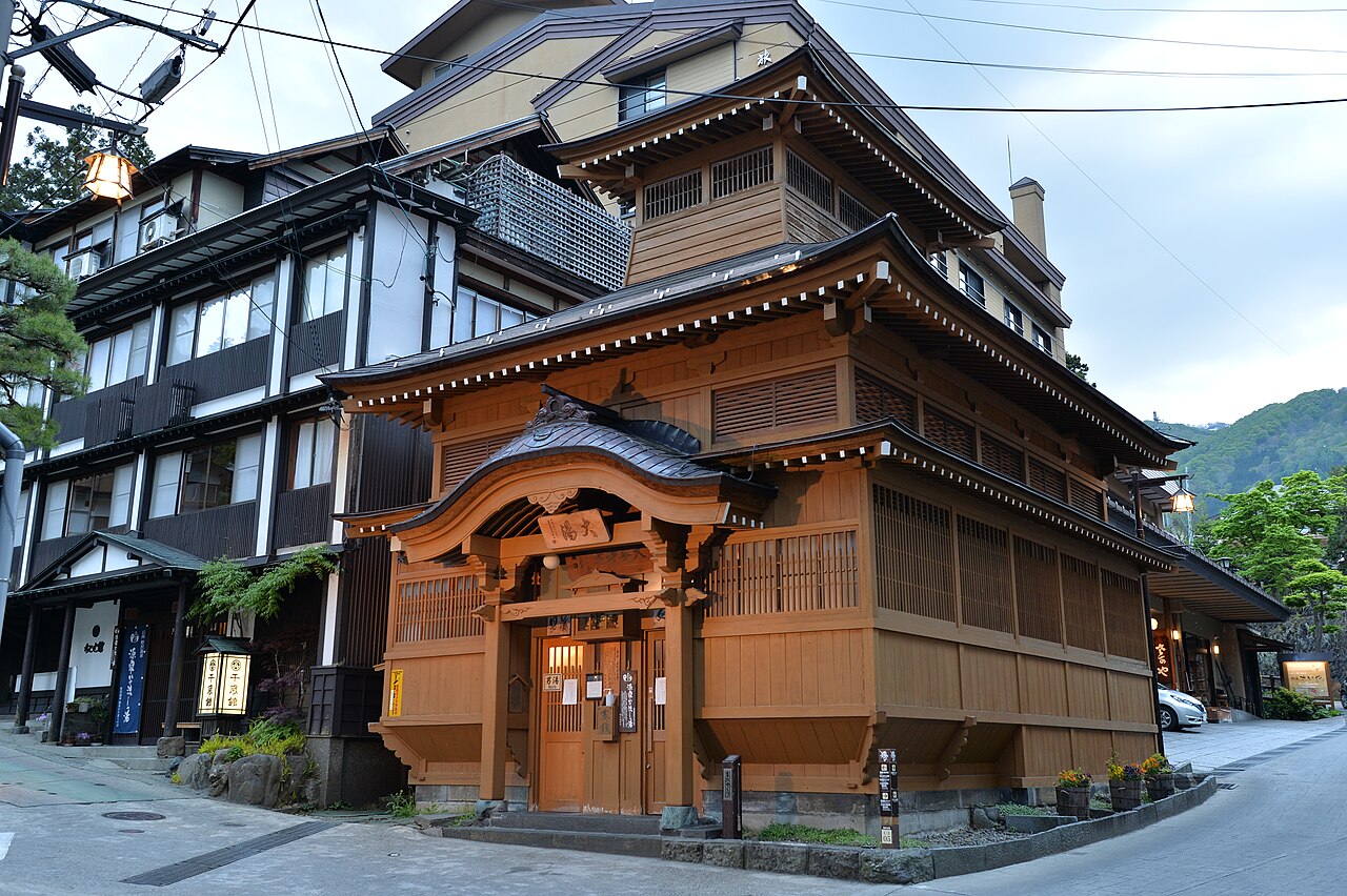 The wooden Oyu public bath in Nozawa Onsen, a multi-storey building with a tiled roof beside a village street