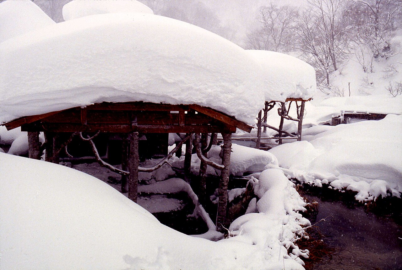 Snow piled thickly on the log-framed roof of an open-air bathhouse at Kuroyu Onsen, Nyuto Onsenkyo