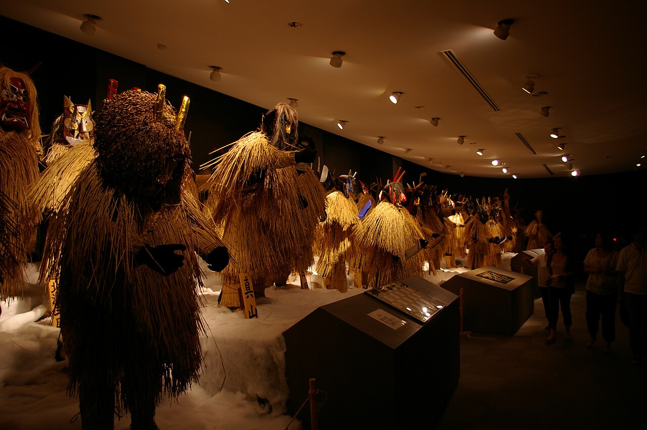 Life-size straw-clad Namahage figures with demon masks lined up in a dim exhibition hall at the Namahage Museum in Oga, Akita.