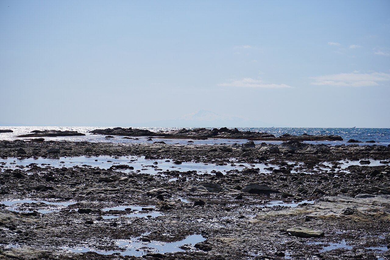 Flat rocky tidal shelf with pools of water at Unosaki Coast on the Oga Peninsula, with a faint mountain on the distant horizon.