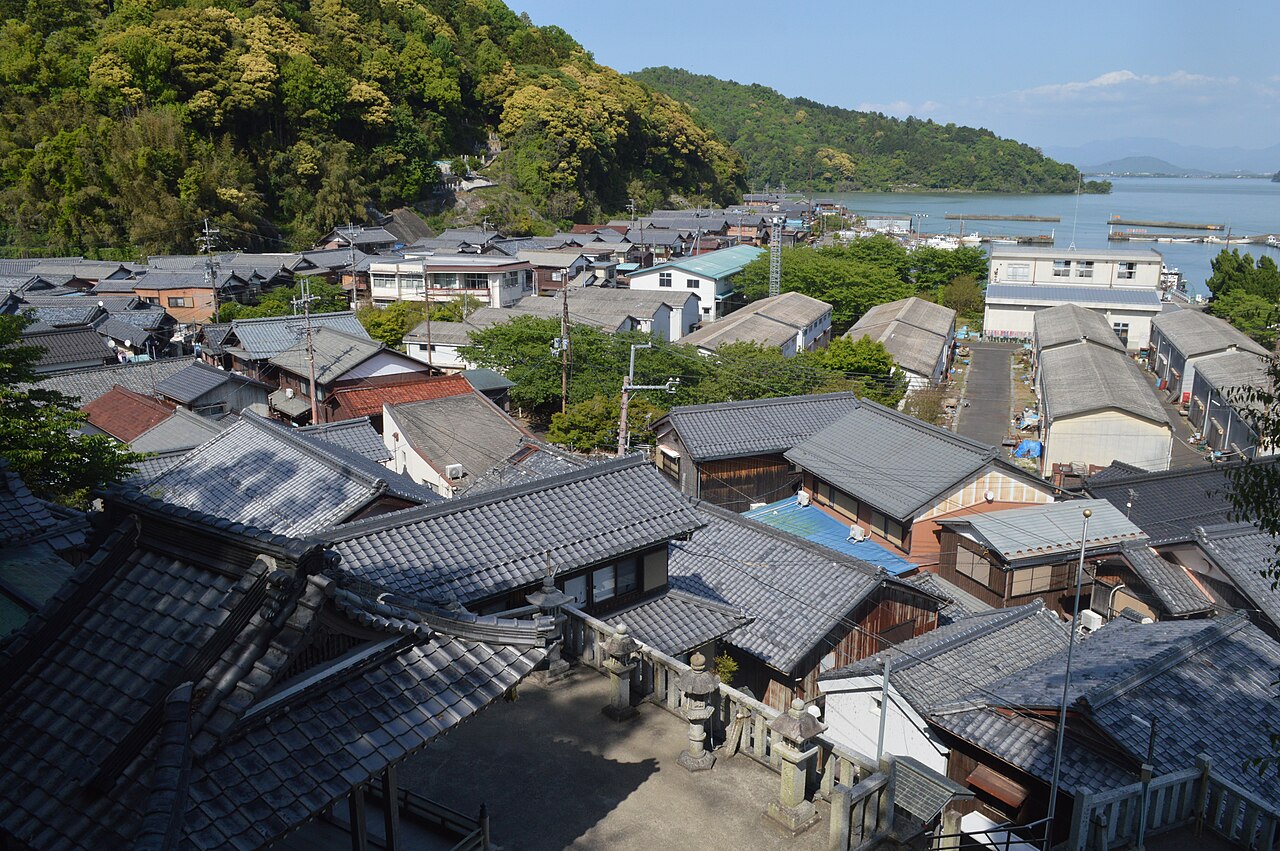 Tiled roofs of the fishing village on Okishima seen from above, with Lake Biwa and the far shore beyond.
