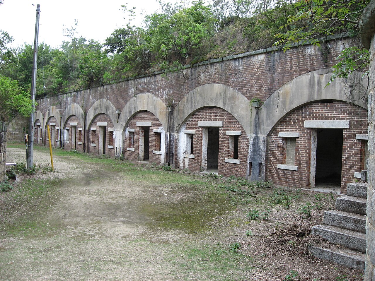 A row of arched brick bays from old gun batteries on Okunoshima, with weeds growing along the top of the earthwork.