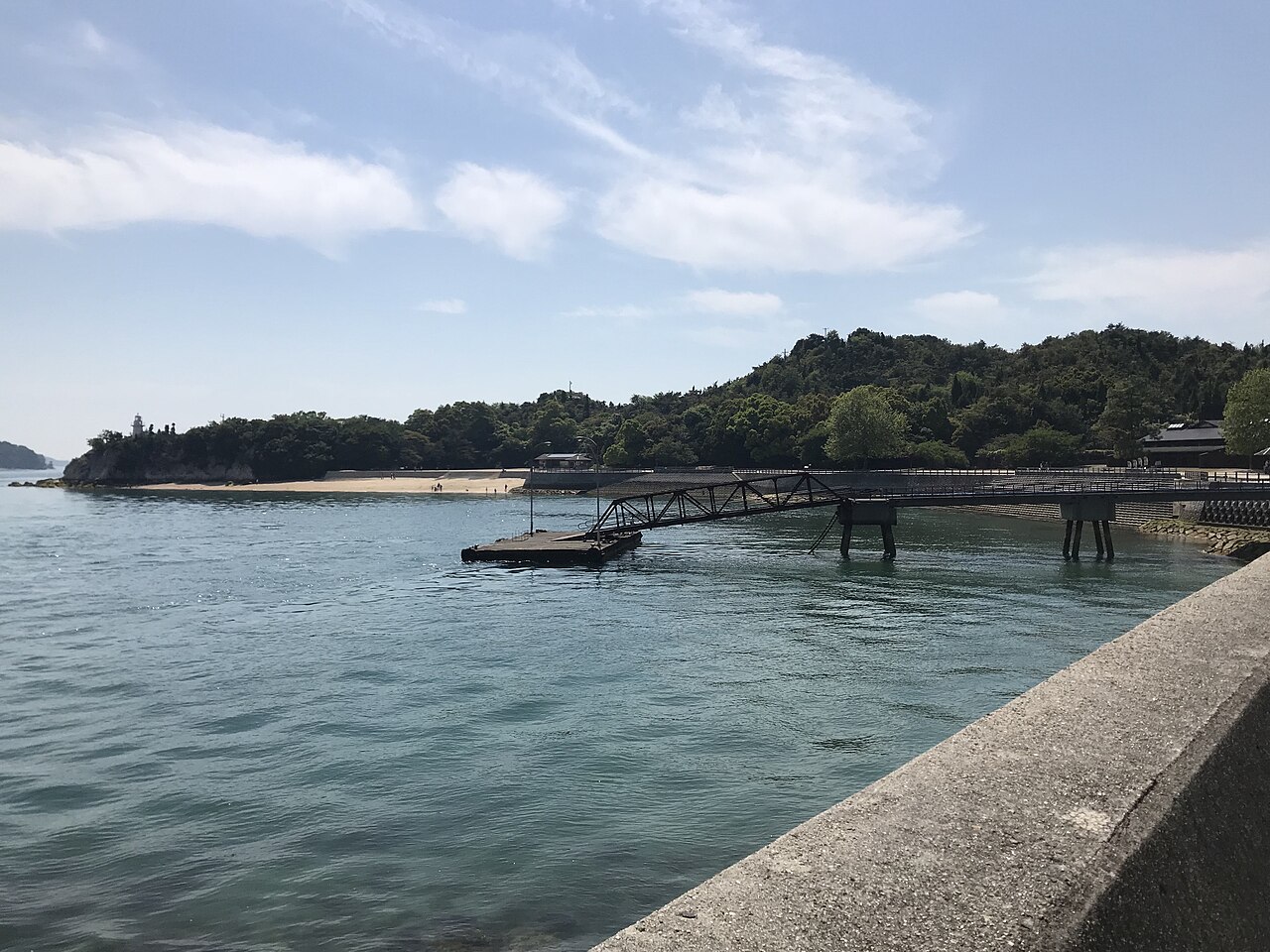 A small wooden pier and wooded shore of Okunoshima seen across calm water of the Seto Inland Sea.