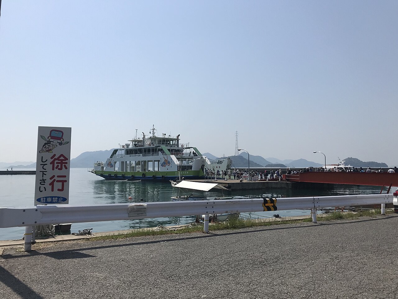 A white car ferry waits at the pier of Tadanoumi Port in hazy sunshine.