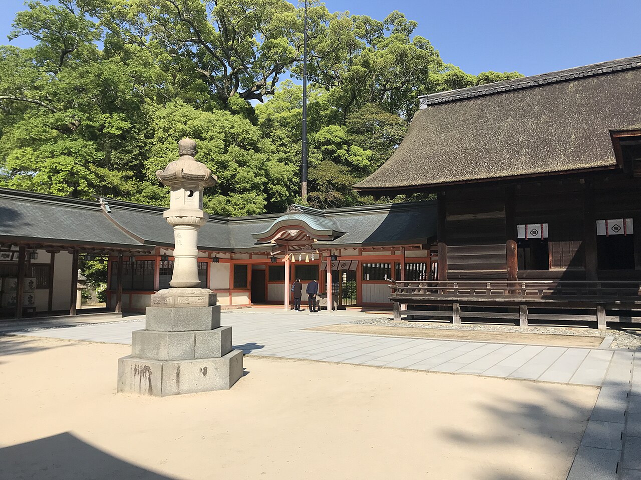 A stone lantern stands in a shrine courtyard in front of a long wooden shrine hall