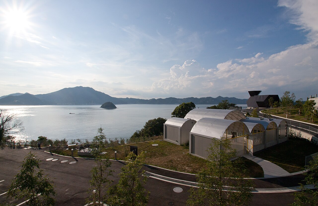 A cluster of low buildings with silver vaulted roofs beside an inland sea dotted with islands