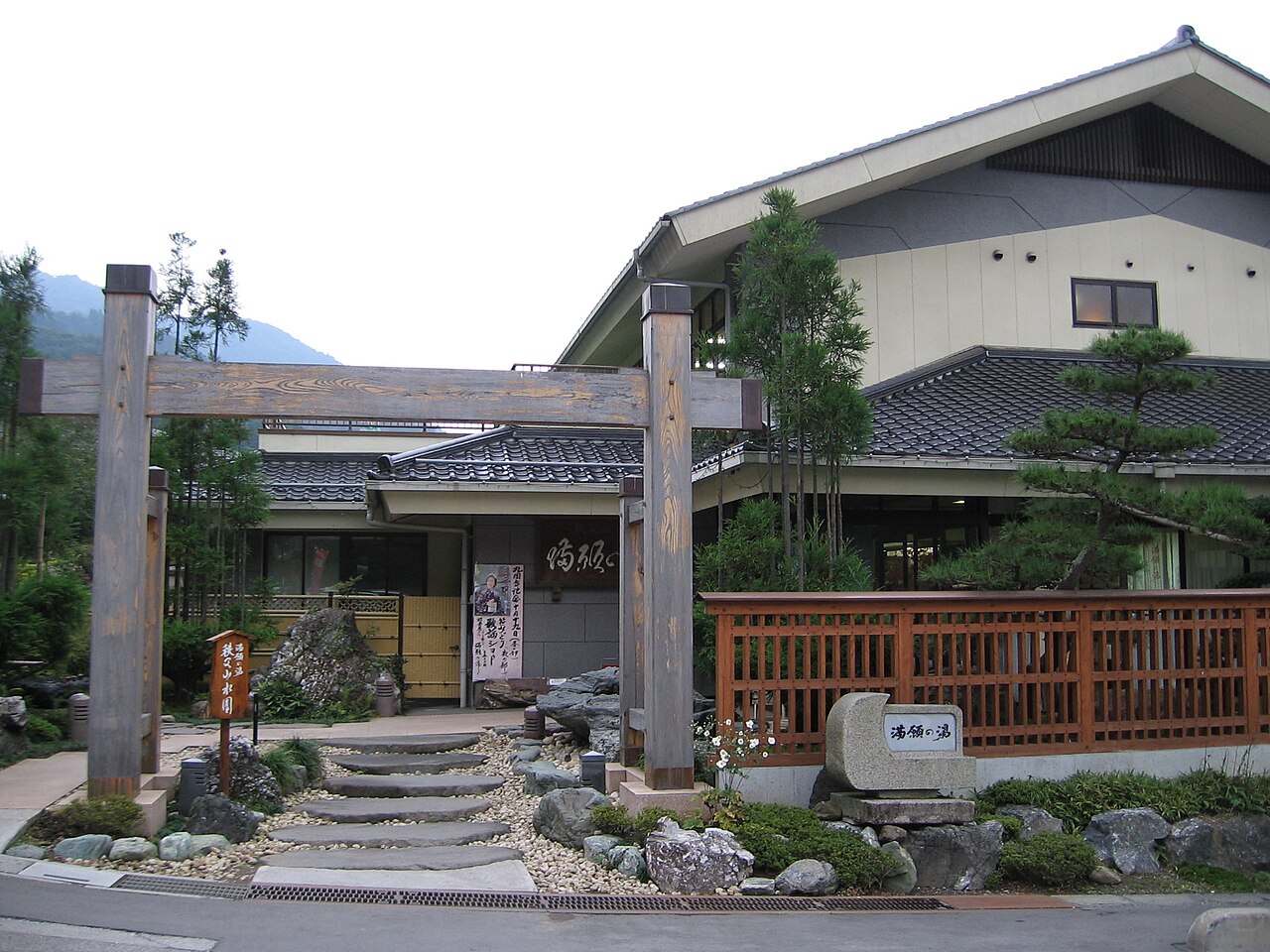 The wooden gate and stone-paved approach to Mangan-no-yu, a hot spring bathhouse in the Chichibu hills.