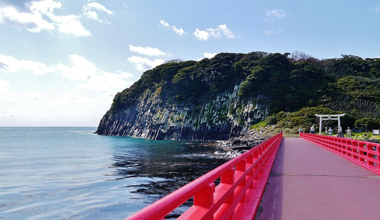 The red-railed bridge to Oshima island, with a torii gate at the far end and the island's rock wall beside it