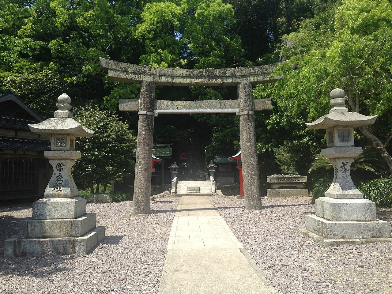 Entrance to the Nakatsumiya approach: a moss-covered stone torii flanked by stone lanterns, with stone steps and a small vermilion shrine building beyond