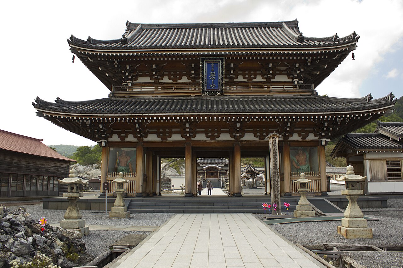 The two-storied wooden main gate of Osorezan Bodaiji temple with stone lanterns and a paved approach