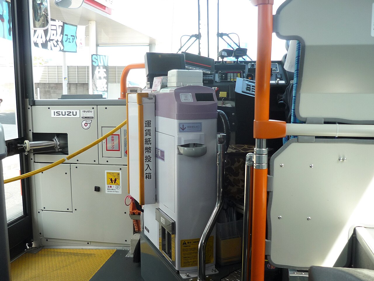 Beside the driver's seat of a local bus: the fare box with its banknote slot, next to the front exit door.