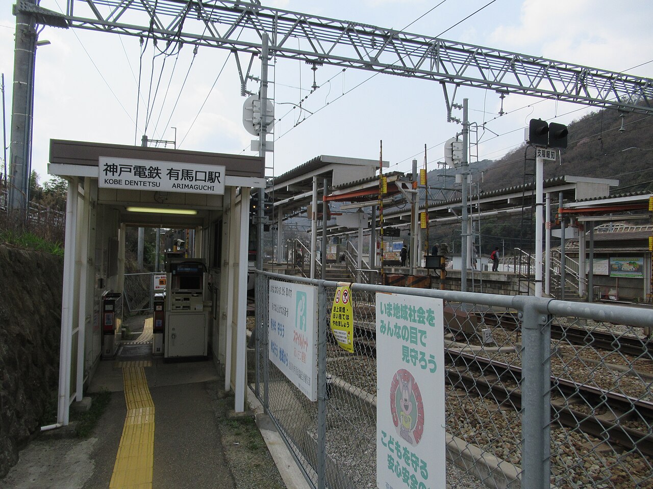 A small hillside station entrance with ticket machines under a simple canopy and the tracks beside it.