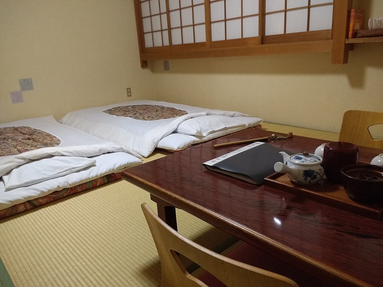 Two futons laid out on tatami mats beside a low lacquered table with a teapot in a Japanese-style guest room at a ryokan in Nara