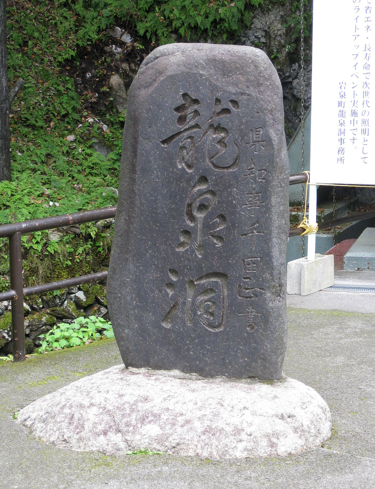 A carved stone monument reading Ryusendo at the cave entrance, with ferns and a handrail behind it.