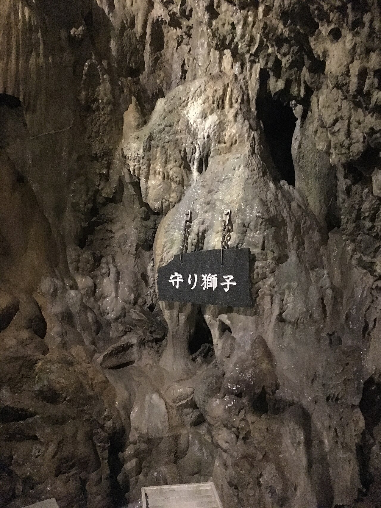 A flowstone formation in Ryusendo Cave labeled Mamori-jishi on a black stone sign hung from the rock.