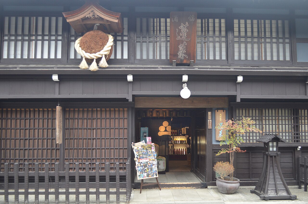 A traditional wooden sake brewery storefront in Japan, with a sugidama cedar-ball sign hanging above the entrance and bottles visible inside.