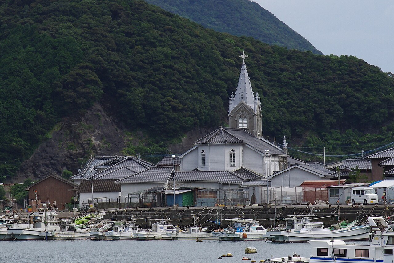 Fishing boats in Sakitsu harbor below the church spire and forested hills.