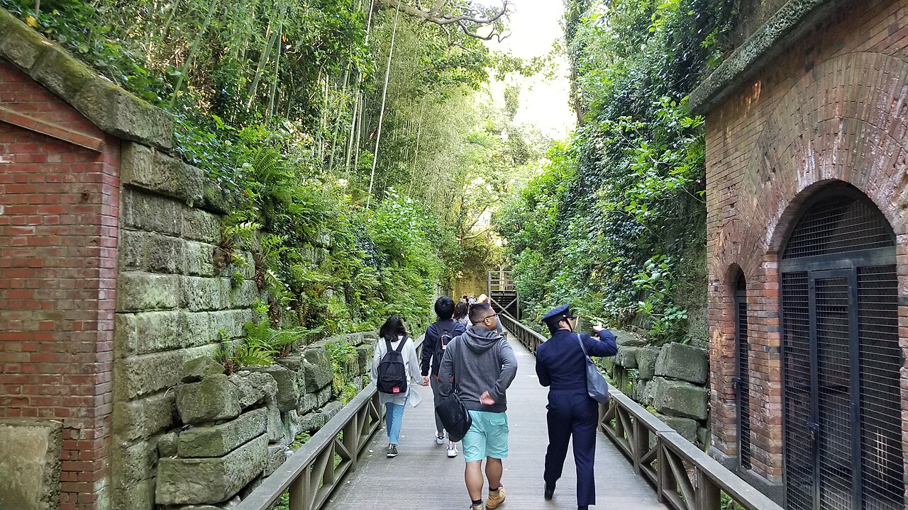 A narrow gravel walkway between old red-brick walls cut into the rock on Sarushima