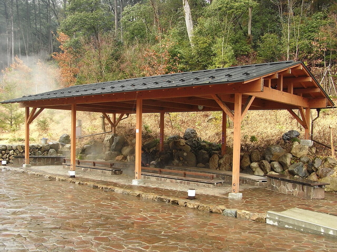 The covered outdoor footbath at Seoto-no-yu, steam drifting over stone paving and long wooden benches beneath a timber roof.
