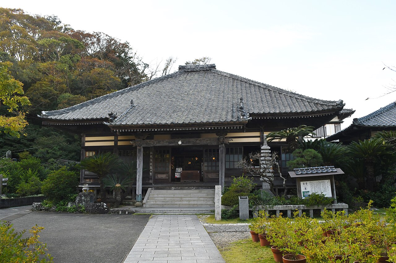 A low tiled-roof temple main hall with a stone-paved path leading to the entrance, surrounded by trees.