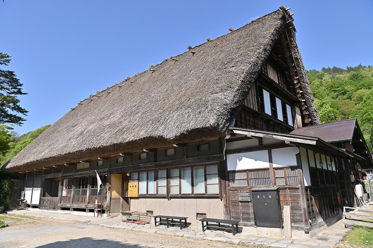 The large thatched roof and timber front of Wada House, a gassho-zukuri farmhouse in Ogimachi, under a clear blue sky