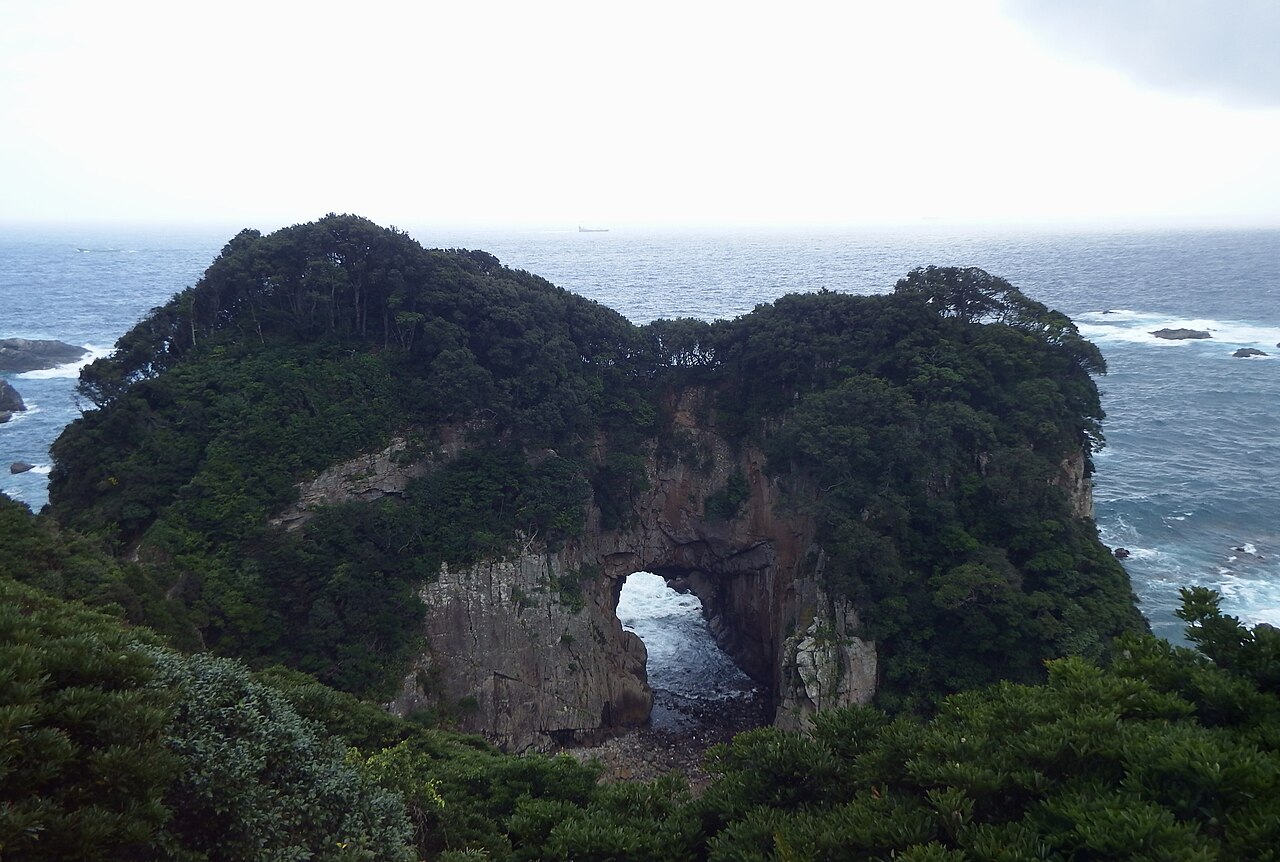 A forested sea cape with a natural rock arch opening onto the ocean at Hakusan Domon