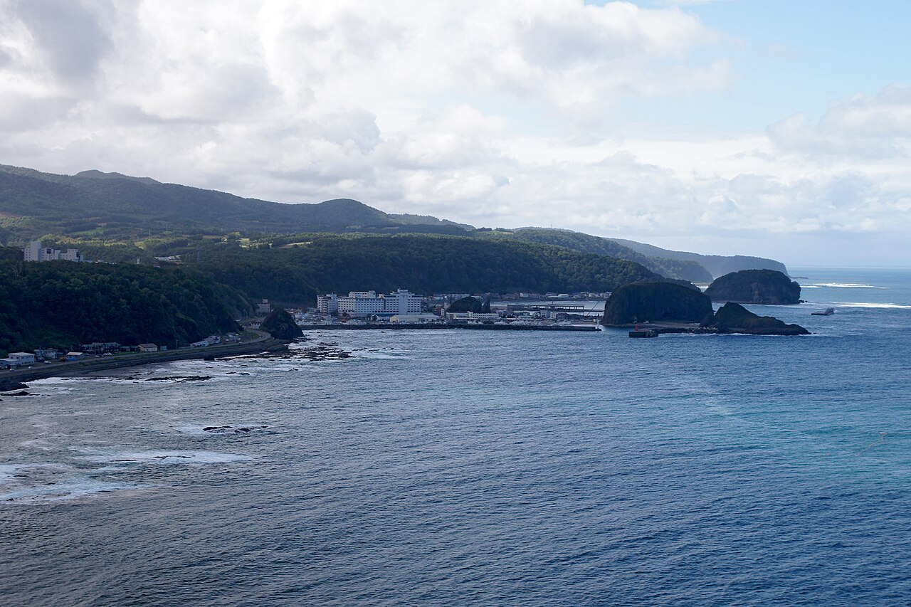 A hazy view over the sea toward a rocky outcrop and a mountainous coast at Utoro.