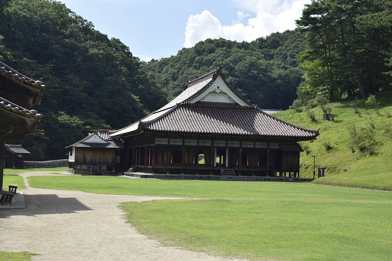 Shizutani School lecture hall with its large tiled roof and open wooden veranda, seen across a green lawn in summer