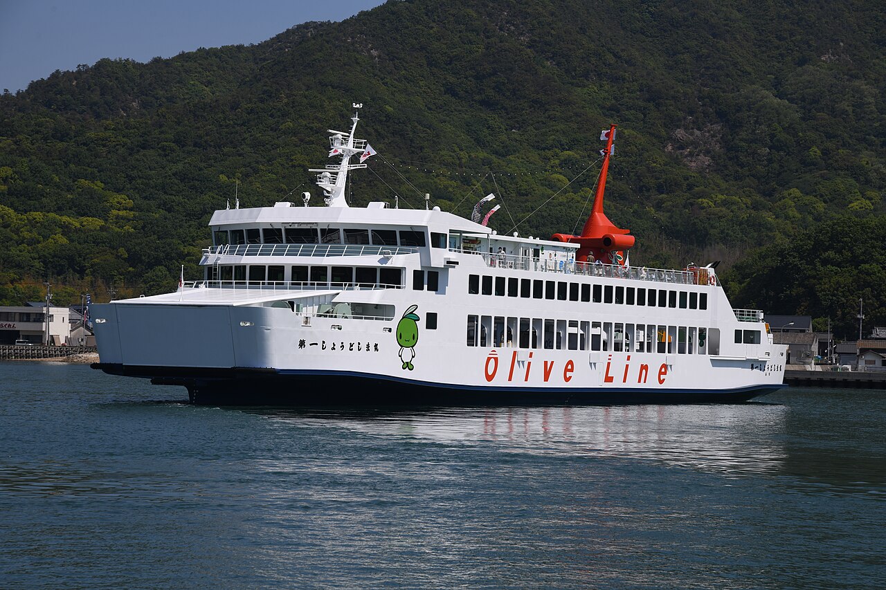 A large white car ferry with a red funnel and Olive Line lettering moving along the coast near Tonosho port.