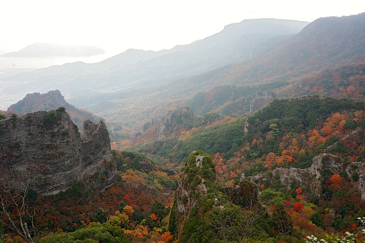 Rocky crags and forested ridges of Kankakei gorge on Shodoshima, with autumn-coloured trees on the slopes and the sea hazy in the distance.