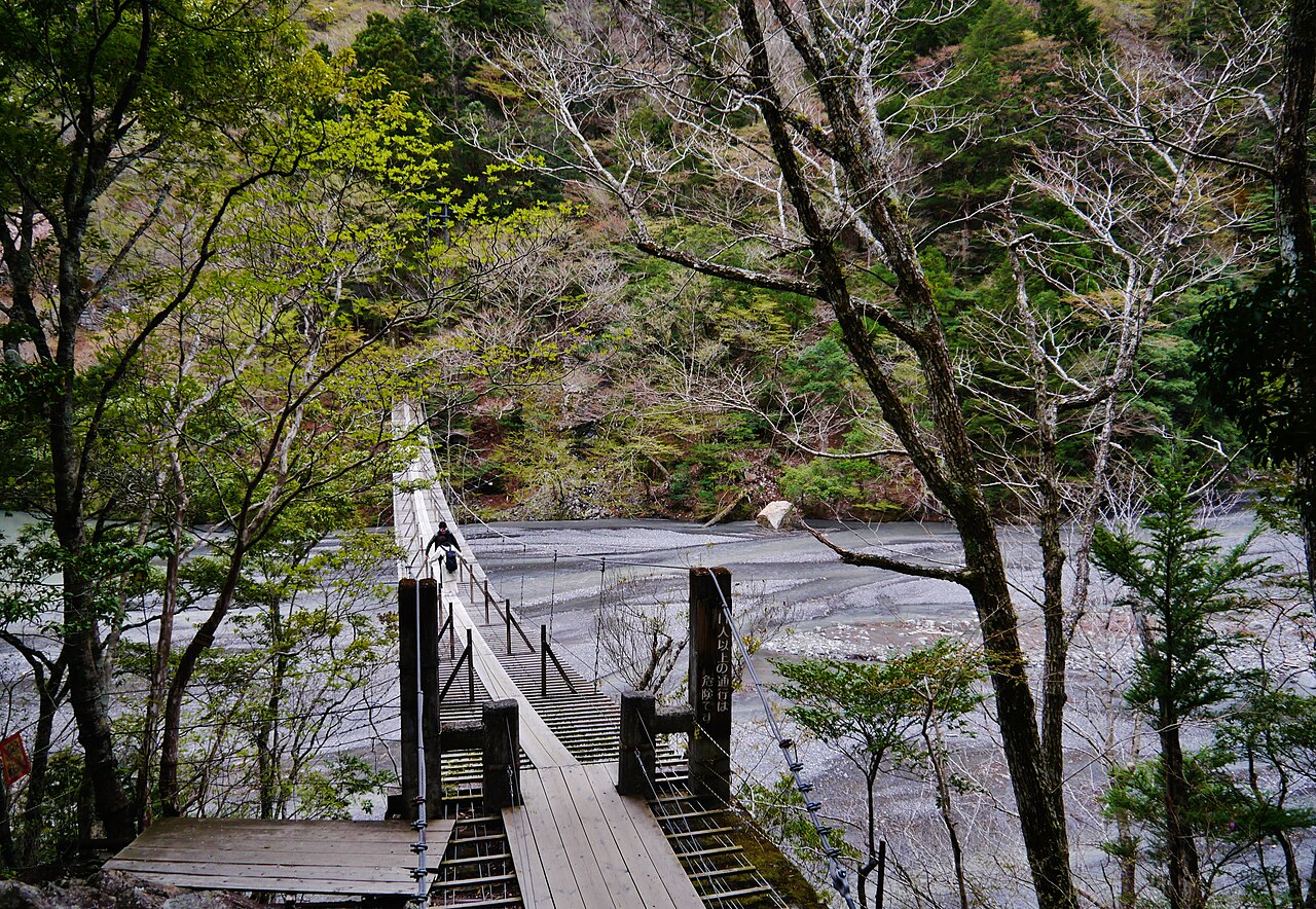 Wooden steps and a gate post leading down onto the Yume no Tsuribashi among bare and budding trees above a wide gravel riverbed