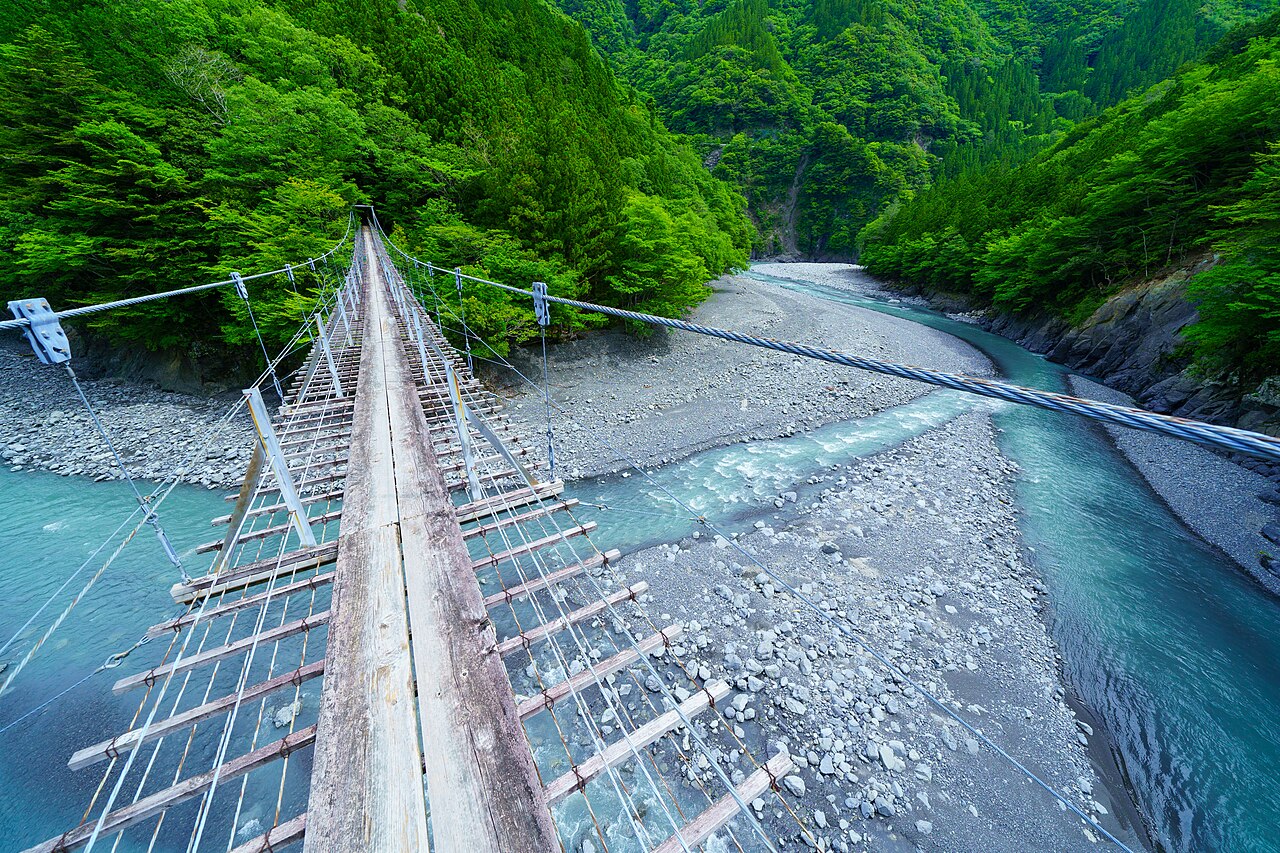 Blue-green river water and pale gravel bars seen from the plank deck of a suspension bridge in Sumatakyo Gorge