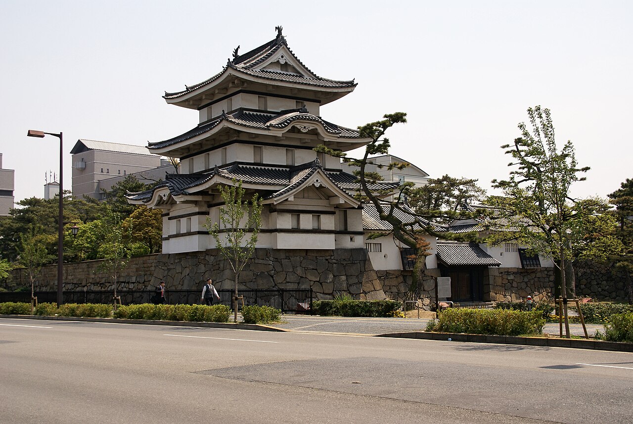 The Tsukimi Turret of Tamamo Park (Takamatsu Castle ruins) beside a road, with pine trees and a stone wall behind