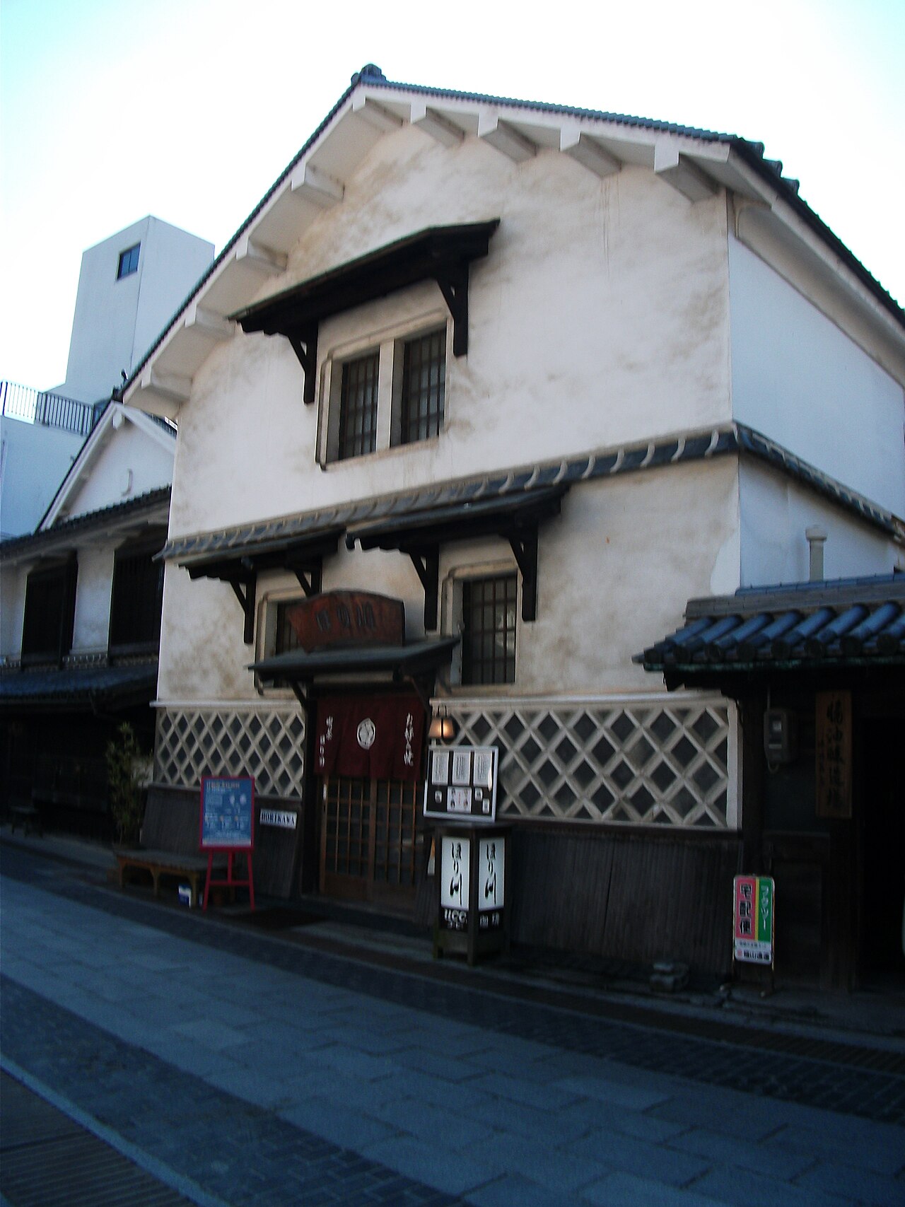 A whitewashed building with latticed windows and a tiled awning along a street in Takehara's preserved townscape