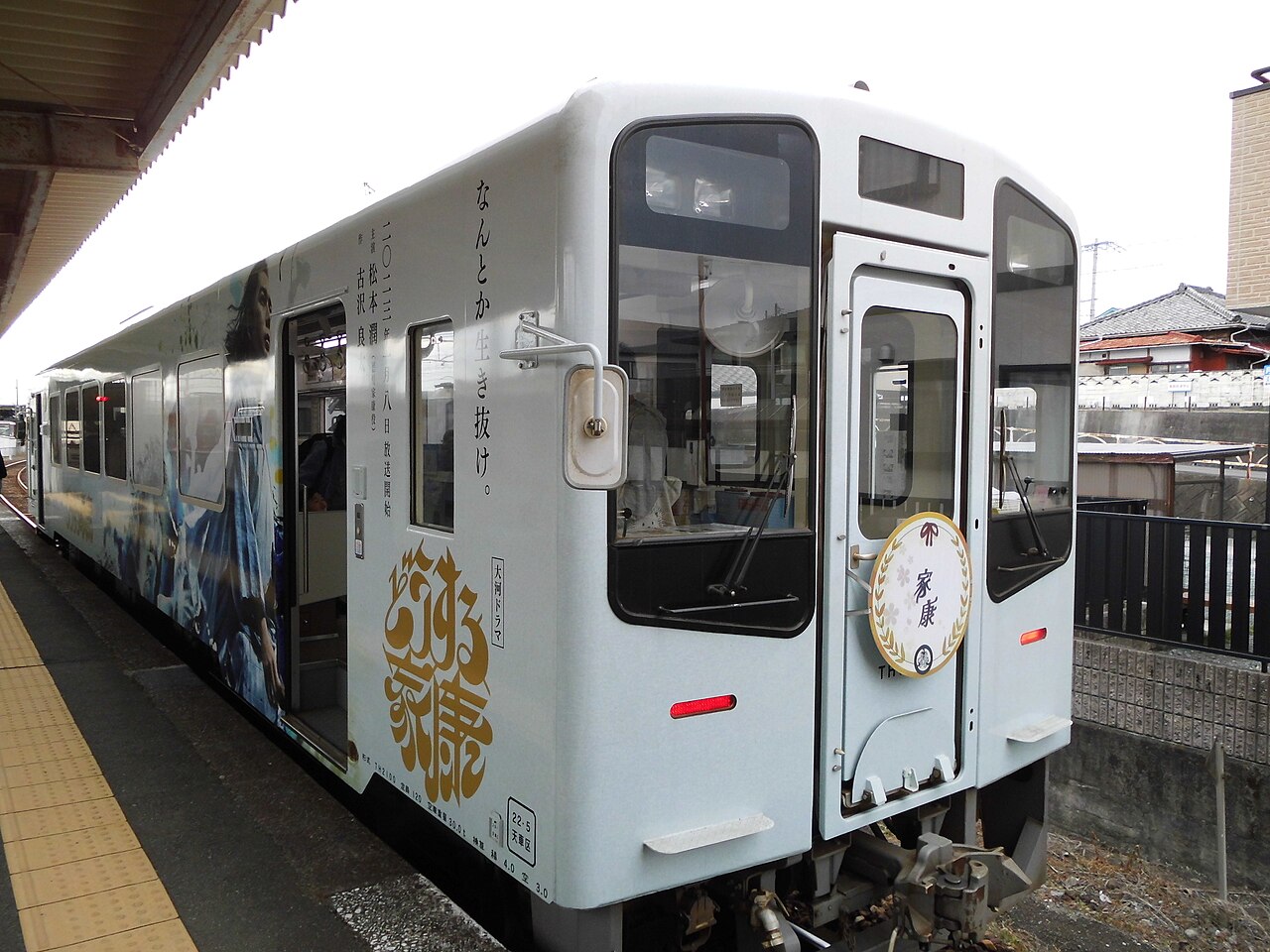A white Tenryu Hamanako Railroad railcar wrapped in a Tokugawa Ieyasu design standing at a platform