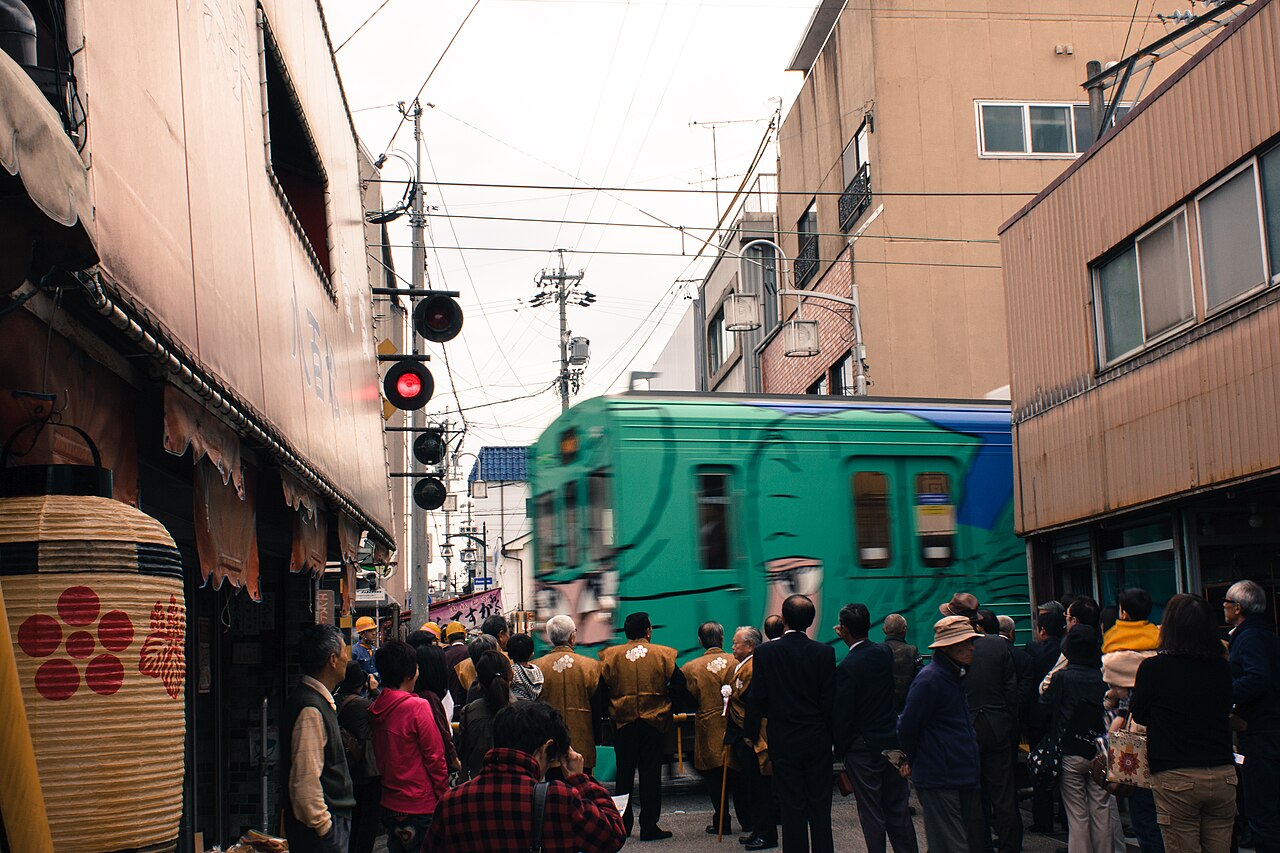 The Ninja train crossing a street in Ueno on the day of the Ueno Tenjin Festival, with onlookers gathered along the road