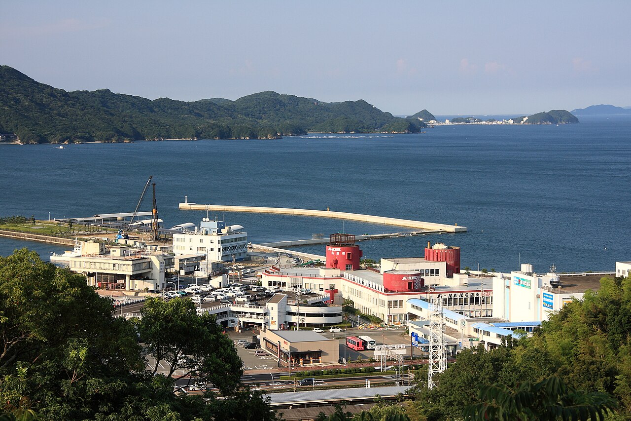 Boats and low waterfront buildings at Sadahama port in Toba with green hills behind the harbour
