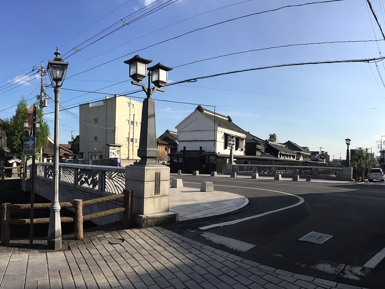 Old-style street lamps on the Koraibashi bridge in Tochigi, with a white-walled storehouse and black fence of the Tsukada museum across the road under a clear sky
