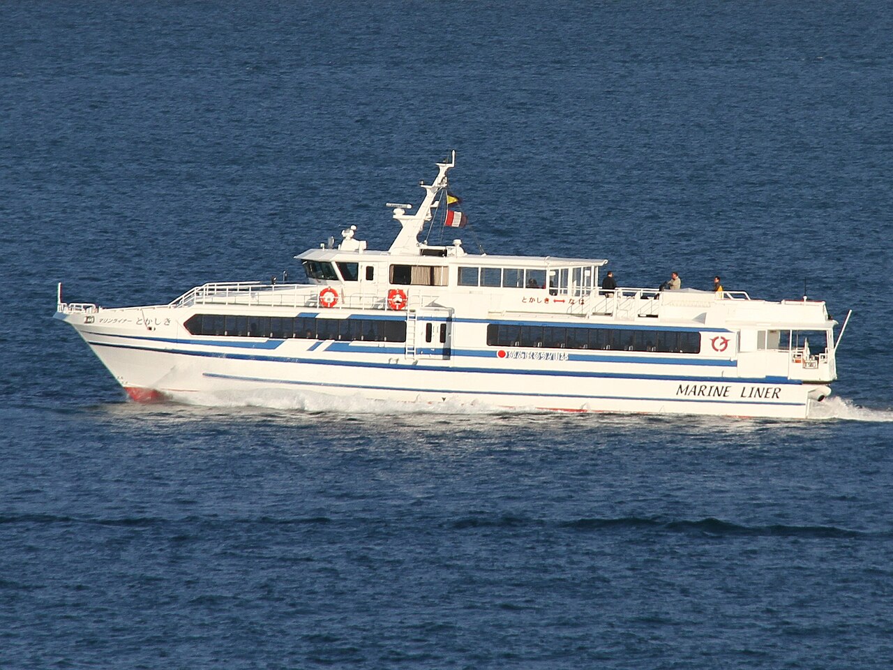 The white high-speed boat Marine Liner Tokashiki crossing blue water, its name painted along the hull