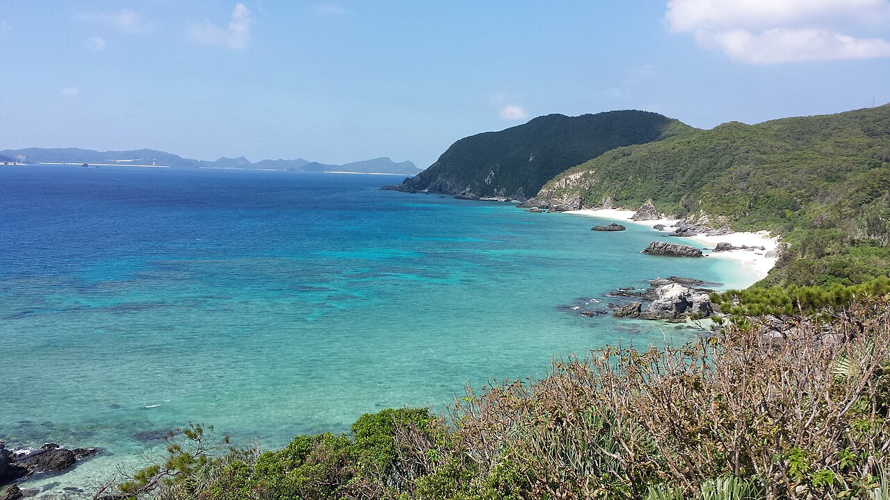 Looking along the coast of Tokashiki Island from the Aharen observation deck, with deep blue water, a pale cove and distant Kerama islands on the horizon