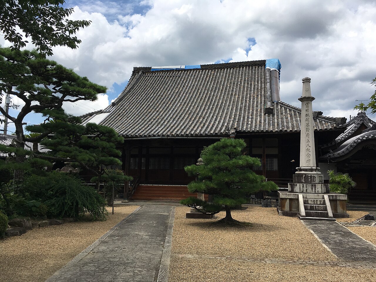 The main hall of Koshoji Betsuin temple in Tondabayashi, a large tiled roof above a gravel courtyard with pine trees and a stone memorial pillar