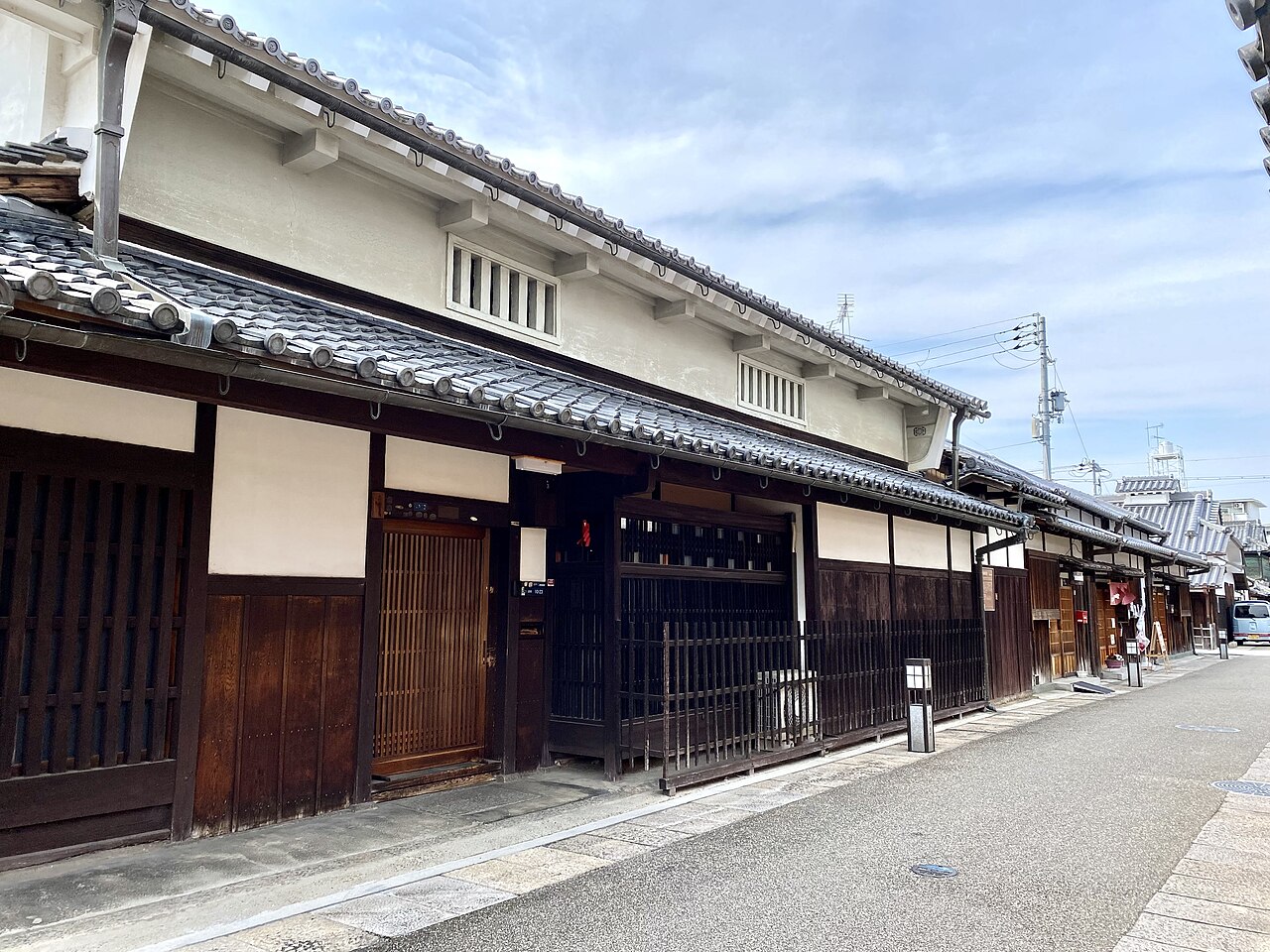 A row of old merchant houses in Tondabayashi's Jinaimachi, with dark wooden lattice fronts, white plaster upper walls and tiled eaves along a paved street