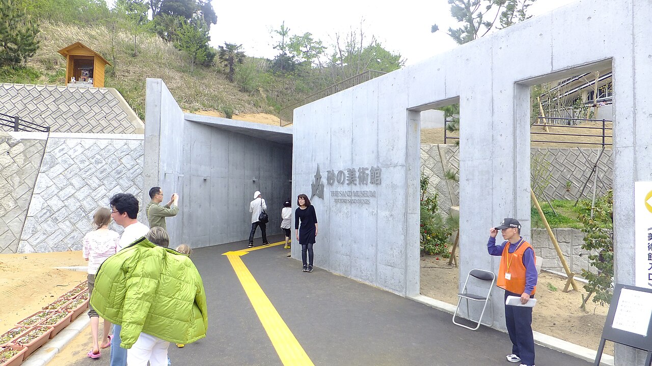 Visitors walking through the Sand Museum's concrete entrance passage beside its carved sign