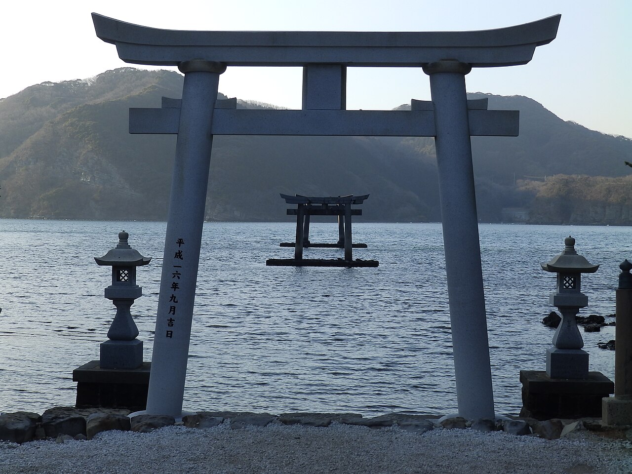 A granite torii on the shore frames a second torii standing in the water of Asou Bay at Watatsumi Shrine, Tsushima