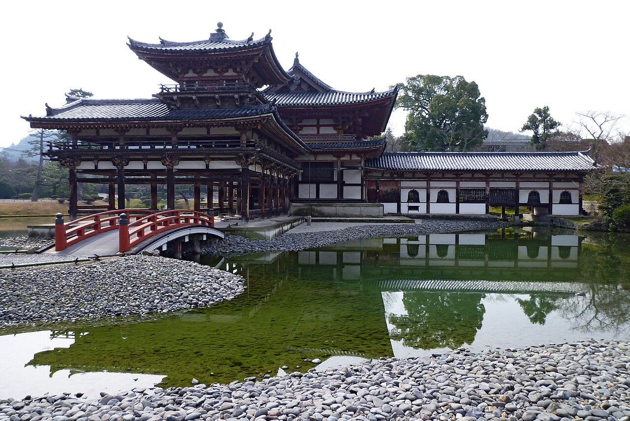 The Phoenix Hall of Byodoin seen from the pond shore with a small red bridge and gravel bank in the foreground