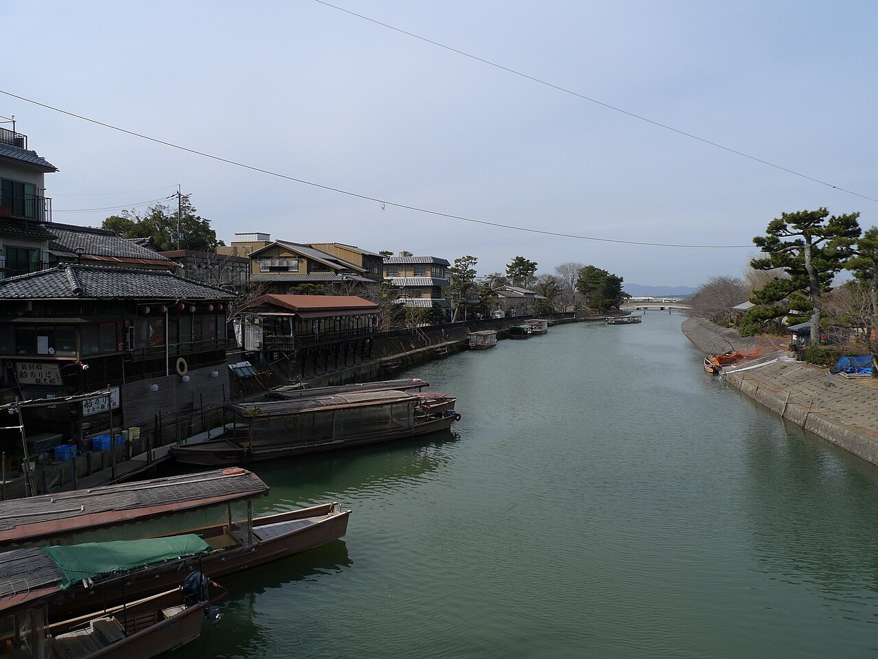 Wooden boats moored along the Uji River with traditional buildings on the left bank