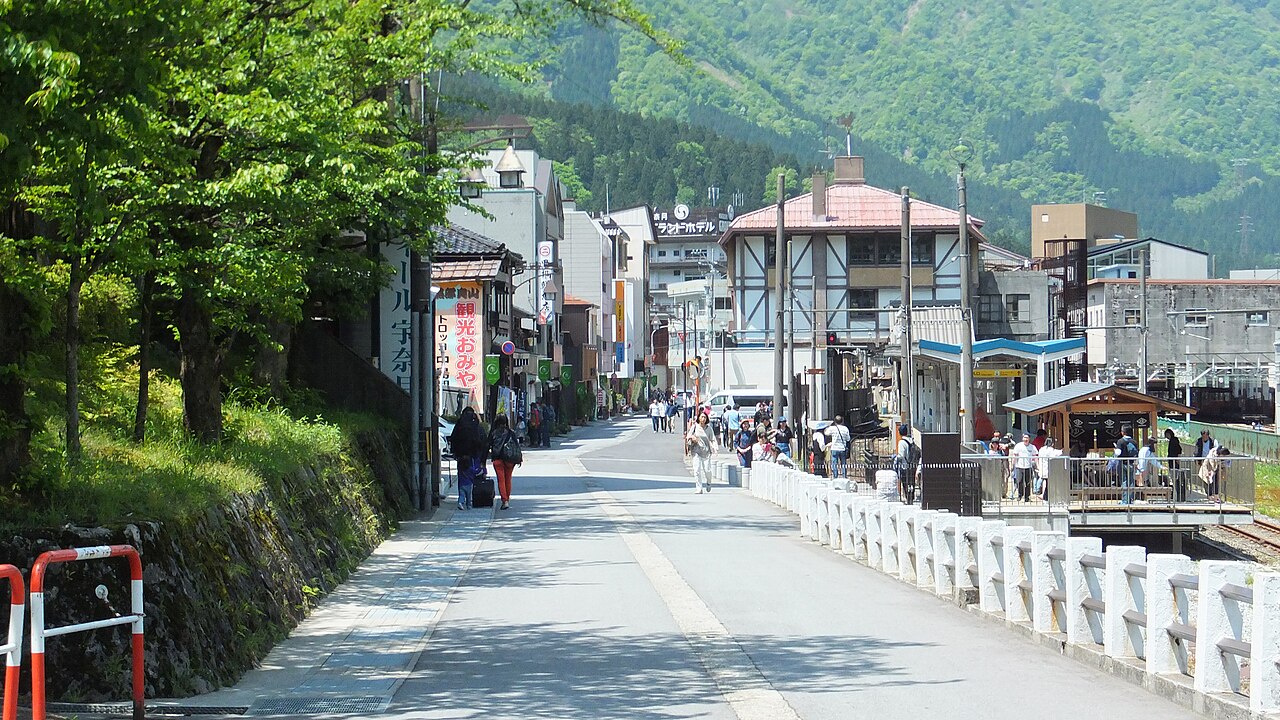 A quiet street in Unazuki Onsen leads past souvenir shops and a half-timbered building toward the end of the road, with forested mountains behind