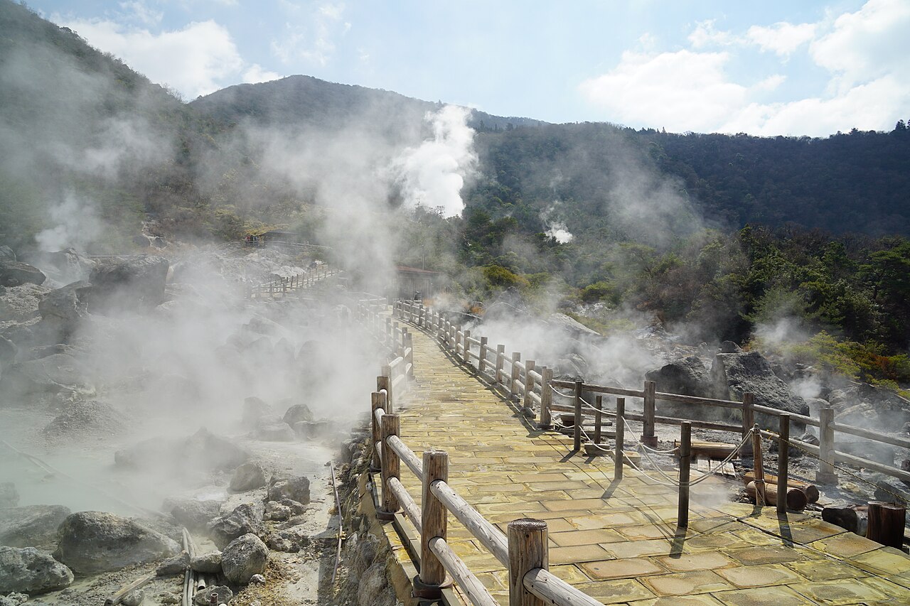 Wooden boardwalk winding through the white steam and bare rock of the Unzen Jigoku geothermal field