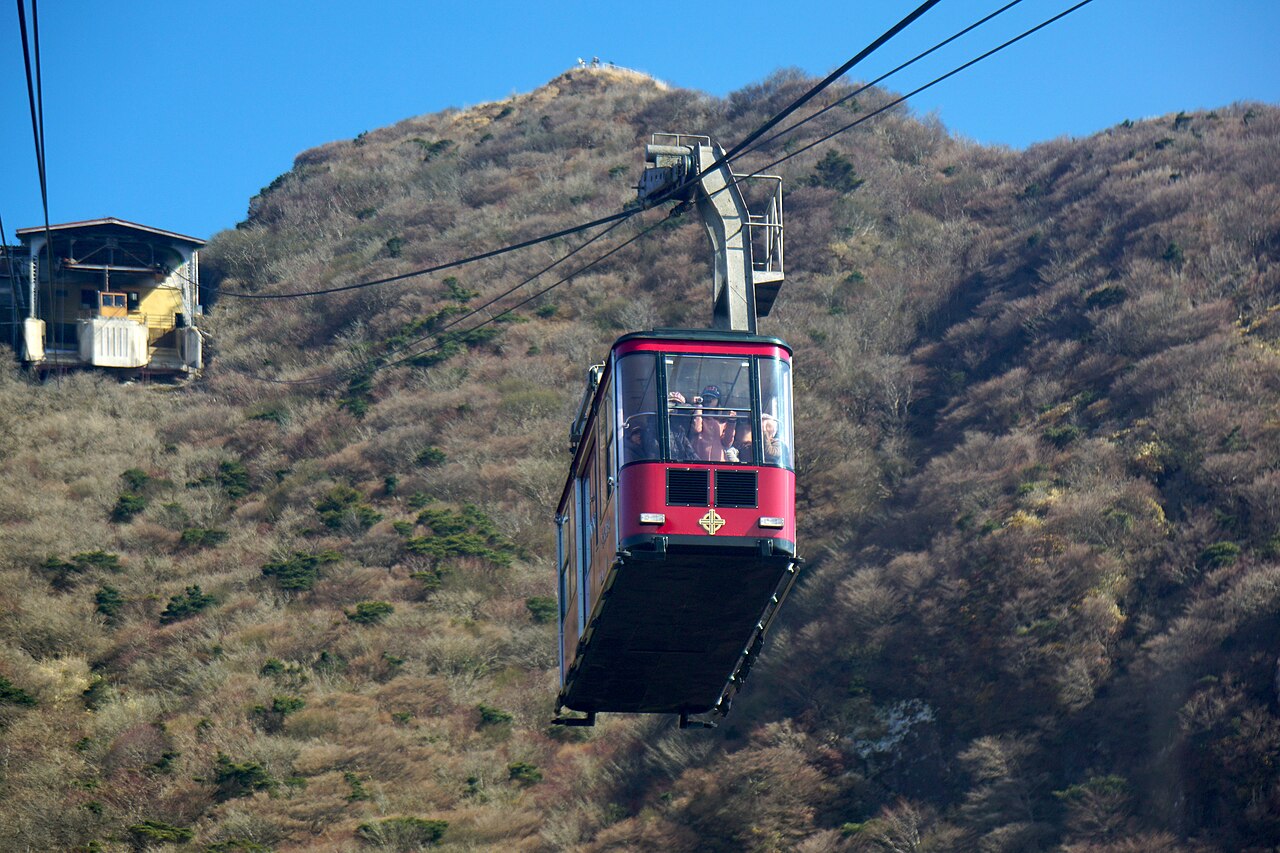 Red Unzen Ropeway cabin rising toward a scrub-covered ridge